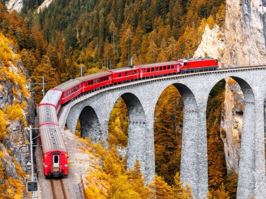 Trem vermelho cruzando o Viaduto de Landwasser, nos Alpes suíços, entre floresta de outono