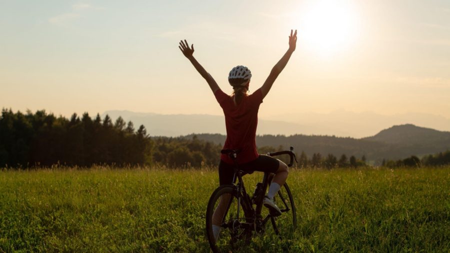 Ciclista de braços erguidos em um campo ao entardecer, no interior da Itália