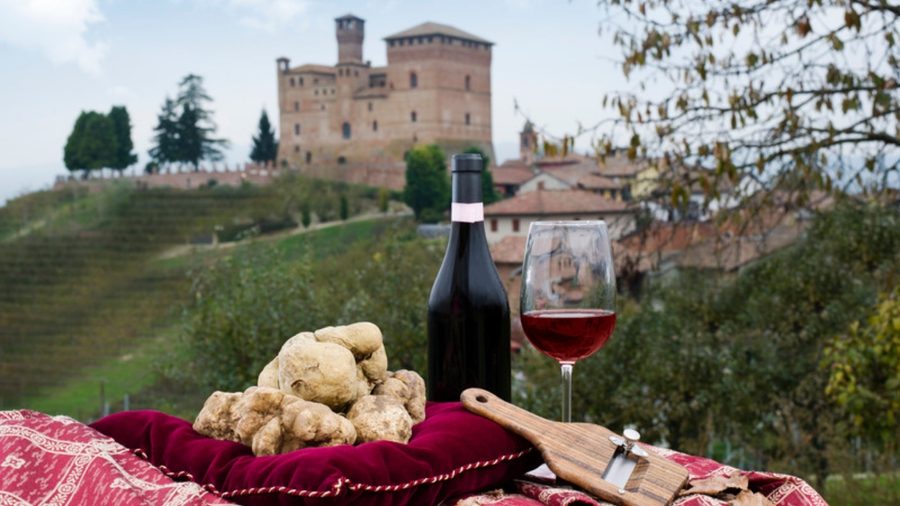 Castelo de Grinzane Cavour ao fundo de vinhedos, com trufa branca, vinho e tábua de queijos em primeiro plano, Langhe