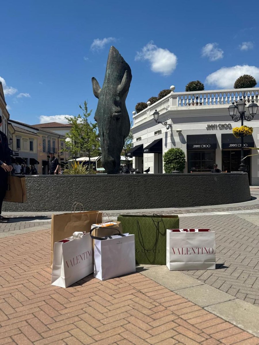 Sacolas de grifes de luxo em frente à escultura do rinoceronte no Serravalle Designer Outlet