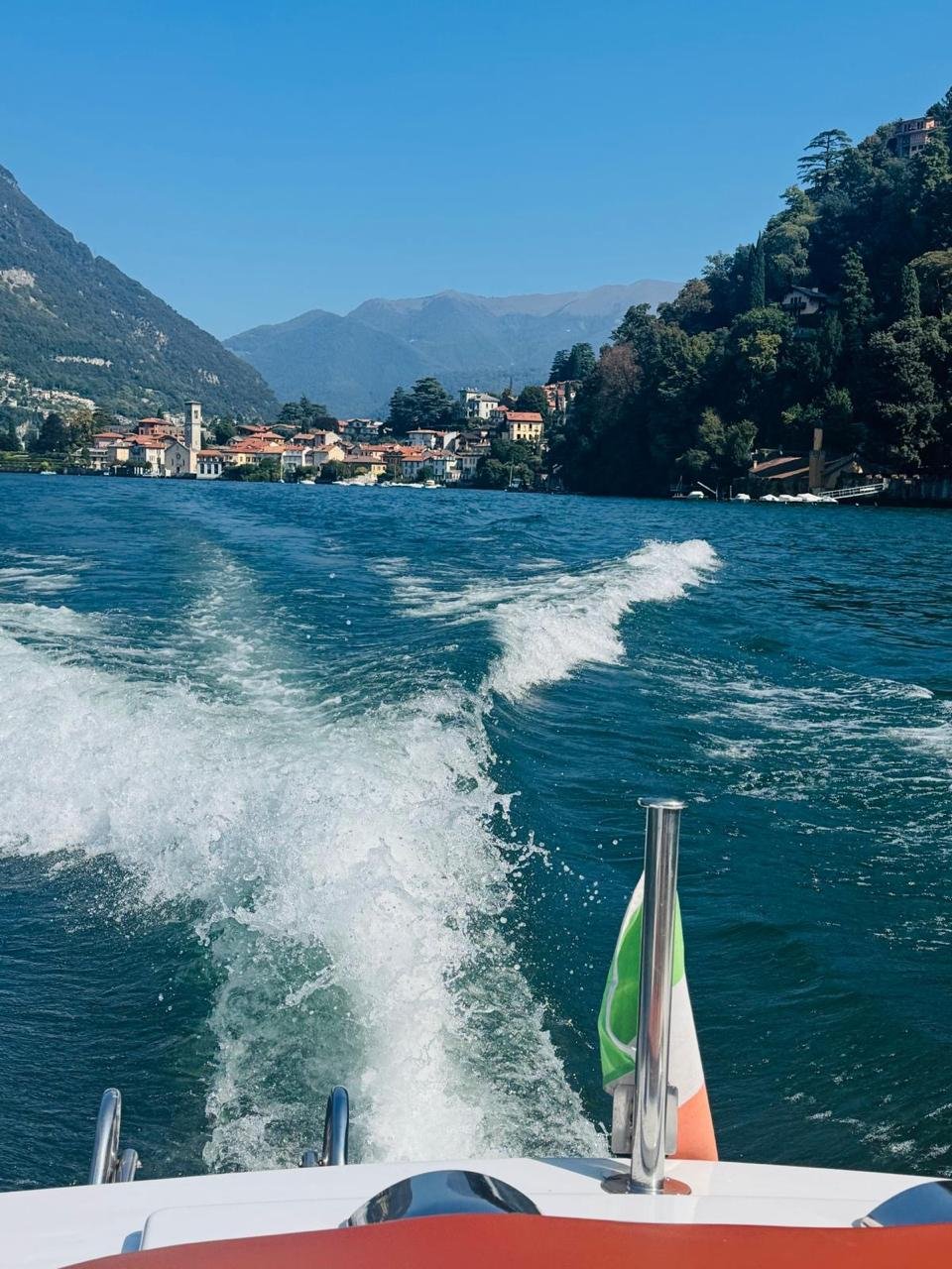 Esteira de um barco no Lago di Como, com um vilarejo à beira d'água ao fundo